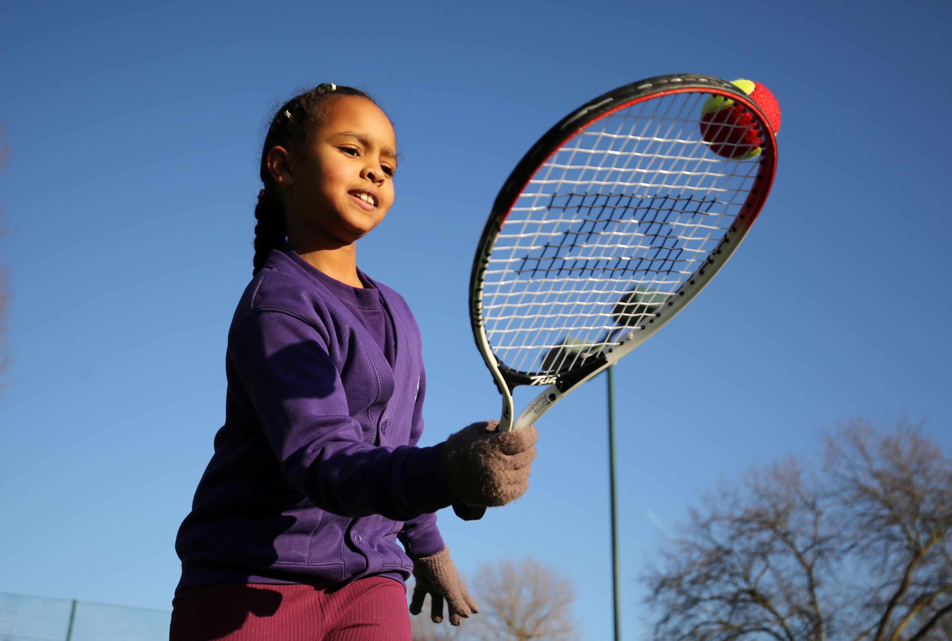 A young girl balancing a tennis ball at the edge of her tennis racket