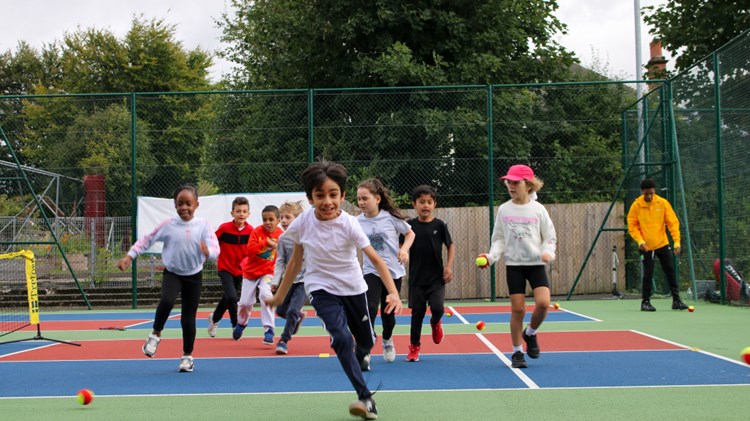 Group of children running towards camera smiling on outdoor tennis court 