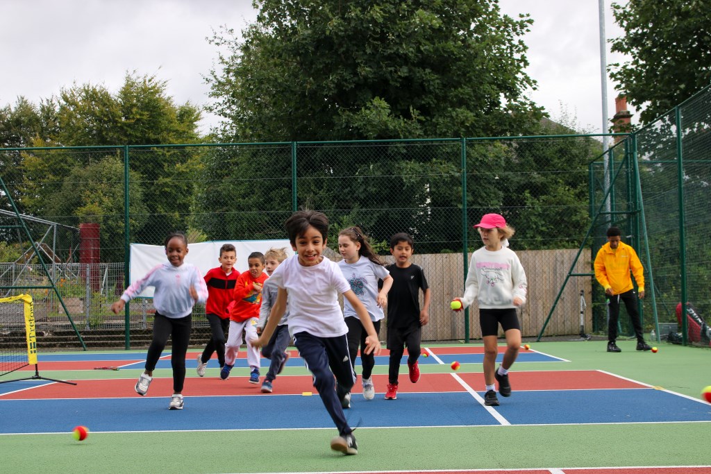Group of children running towards camera smiling on outdoor tennis court 
