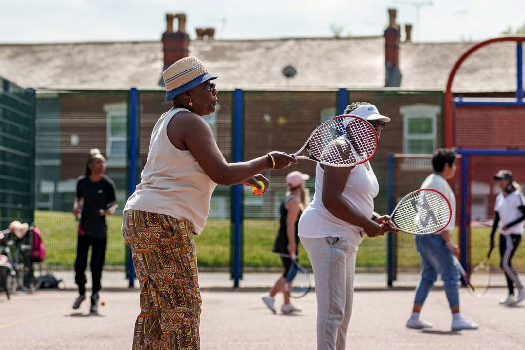 An image of a group of ladies holding tennis rackets and balls on a concrete tennis court group session