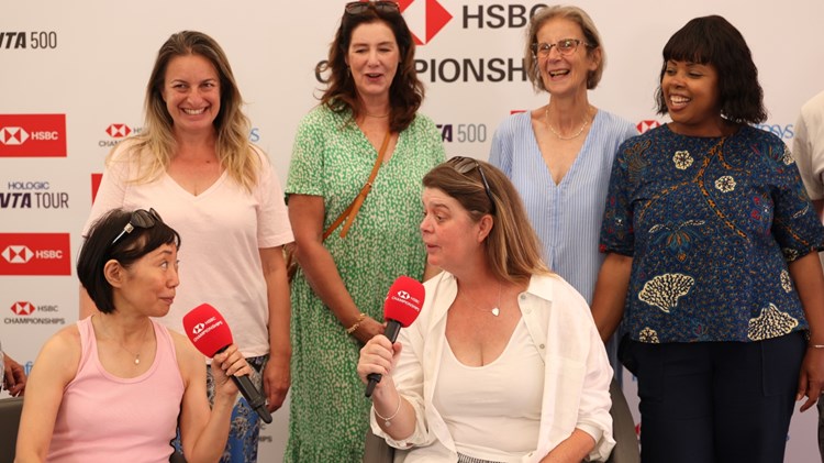 Two women sitting talking into microphones with four women laughing behind