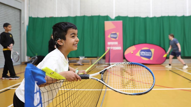 A child leaning over the net with a  racket in hand, smiling.