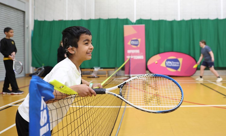 A child leaning over the net with a  racket in hand, smiling.