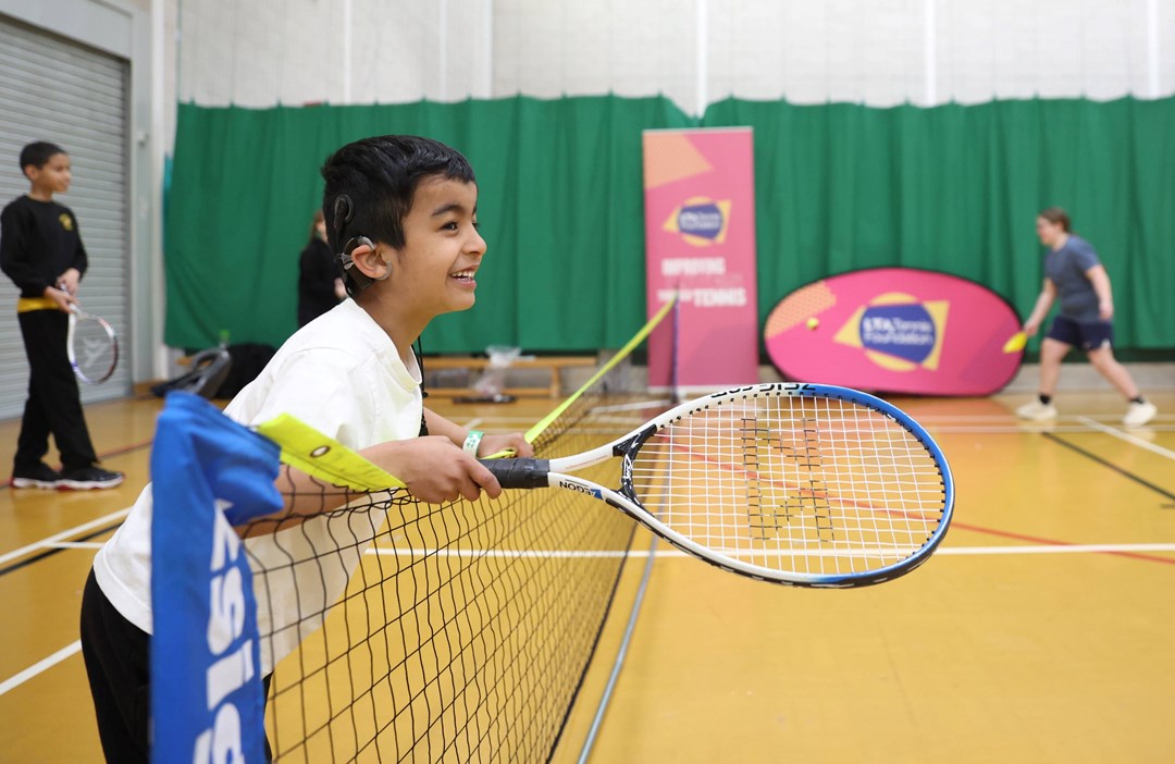 A child leaning over the net with a  racket in hand, smiling.