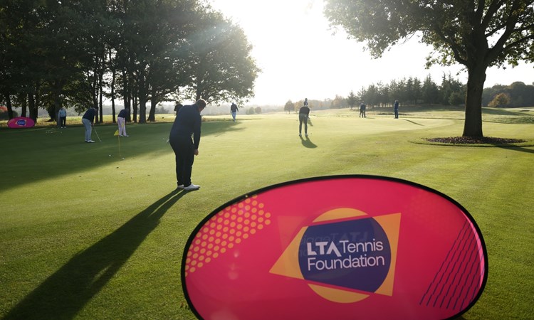 A golf green with an LTA Tennis Foundation banner in the foreground, and people in the background