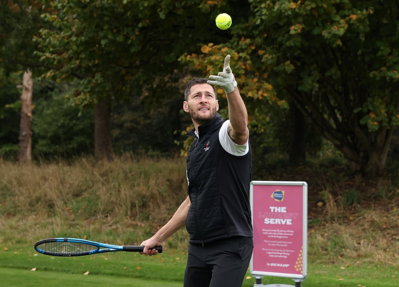 A man throwing up a tennis ball and preparing to hit it with a tennis racket, as part of the Longest Serve competition 
