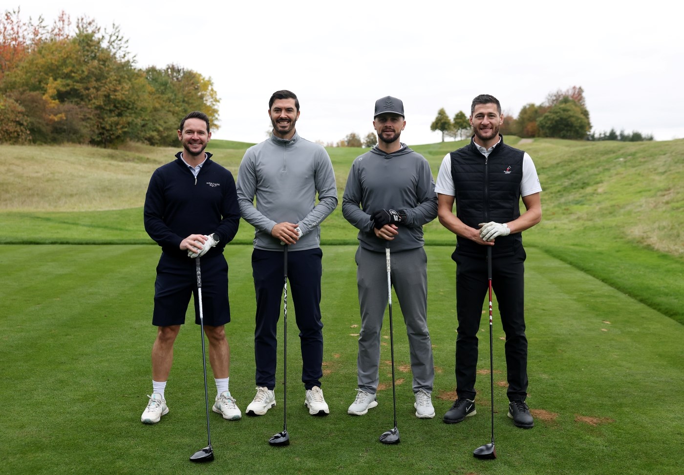 Four men stood in a row on the golf green, holding their golf clubs