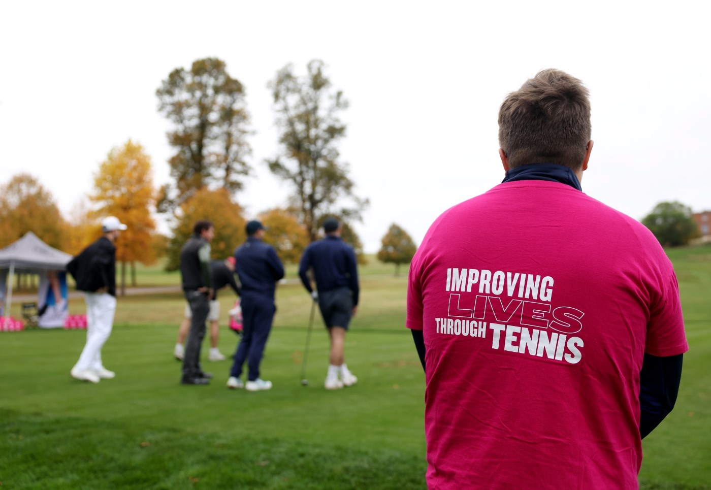 A man photographed from the back, wearing a t-shirt that says 'Improving lives through tennis'