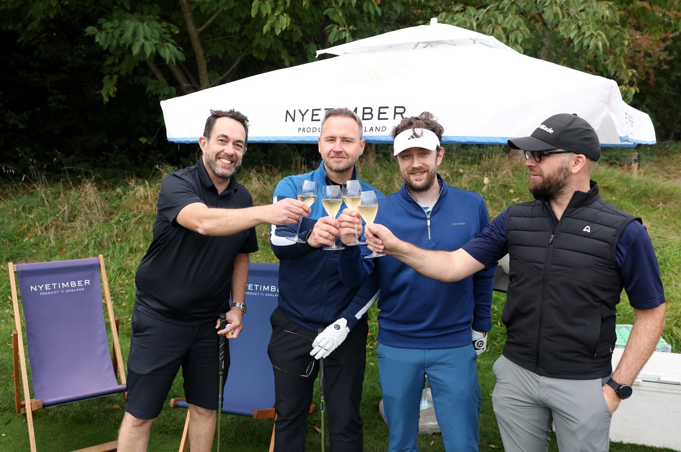 Four men holding glasses of Nyetimber and holding them out to cheers each other
