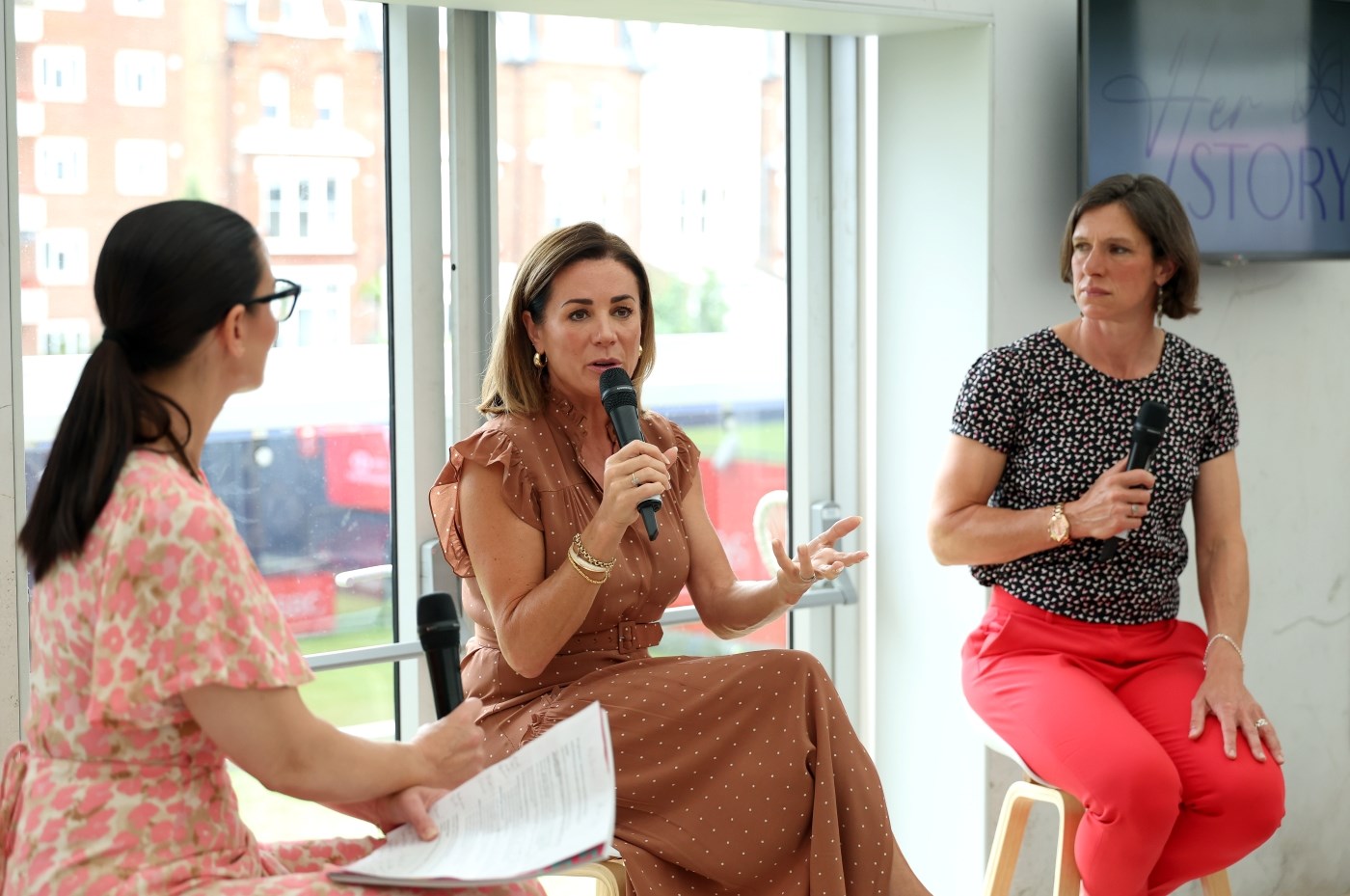 Three women on stools with microphones speaking to each other