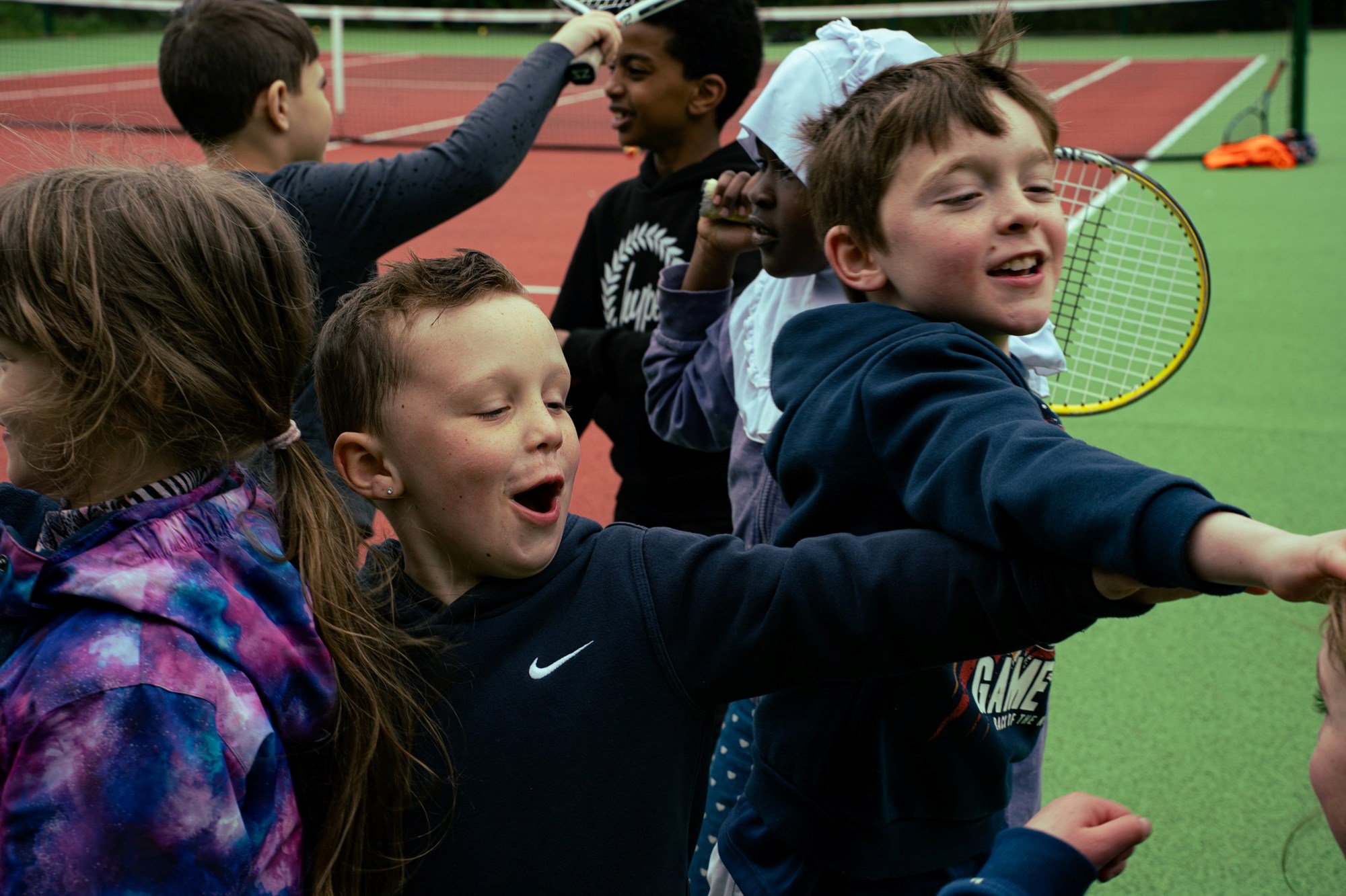 A group of young kids on playing around on court with two young boys at the fronts reaching their arms out and cheering