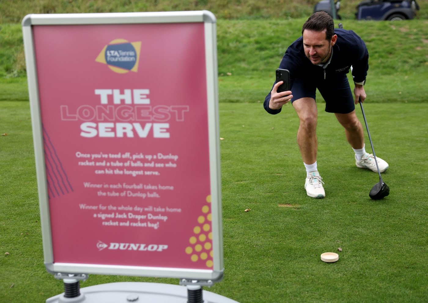 A male golfer bending down to take an image of the LTA TF banner 