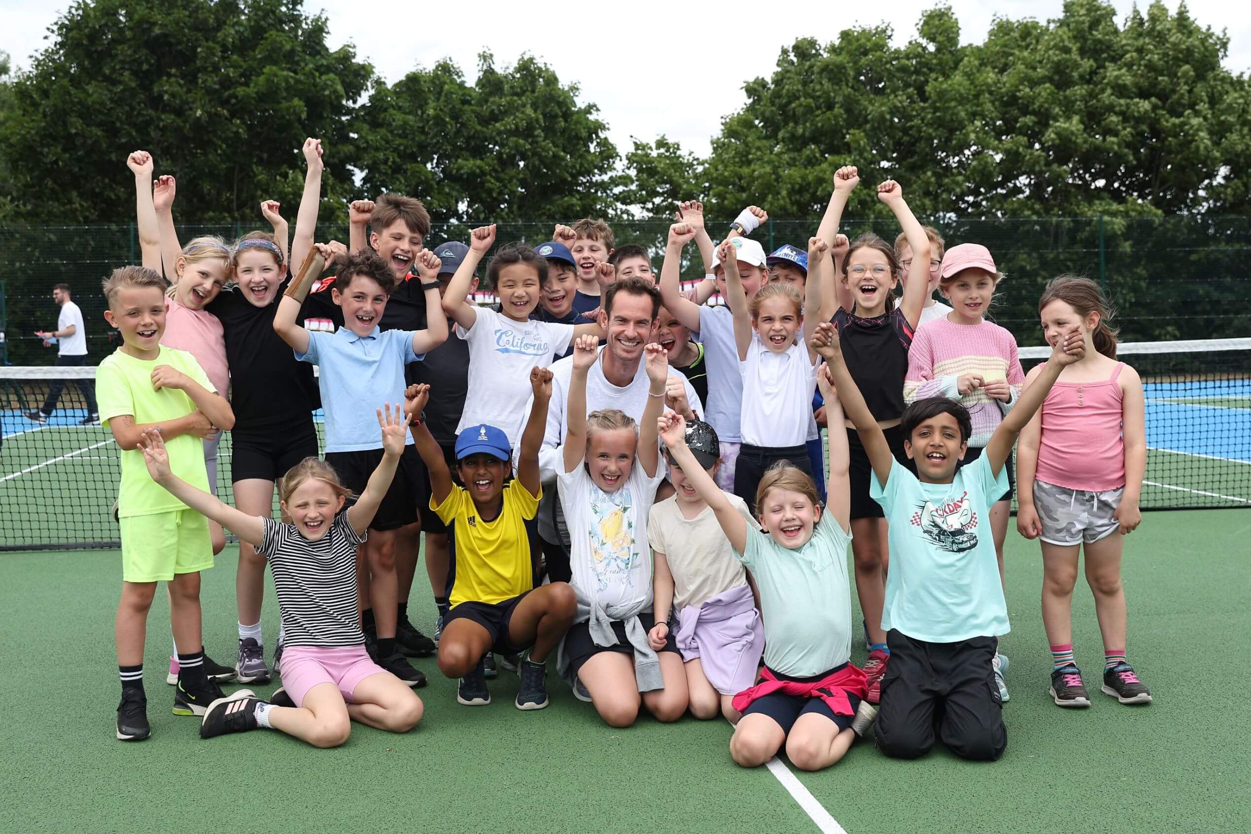 Andy Murray smiling on a park court surrounded by young children smiling and cheering