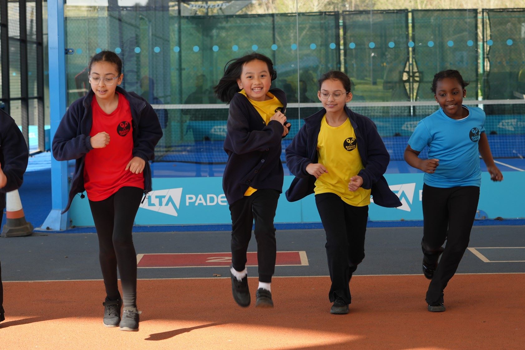 A group of four kids running side by side across a tennis court