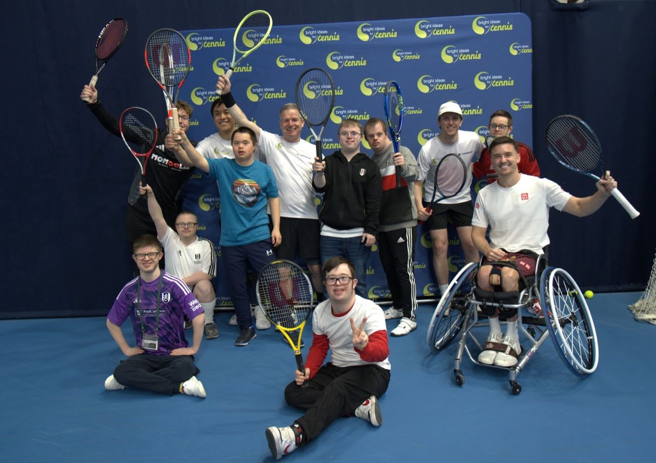 A group of Bright Ideas for Tennis participants with Gordon Reid, holding their rackets in the air