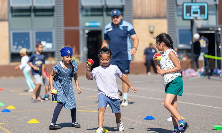 Three young kids playing with tennis balls and cones on the ground while their coach watches on