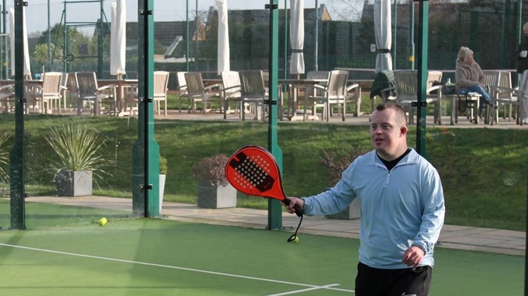 Young disabled man playing padel at a venue with a red padel bat