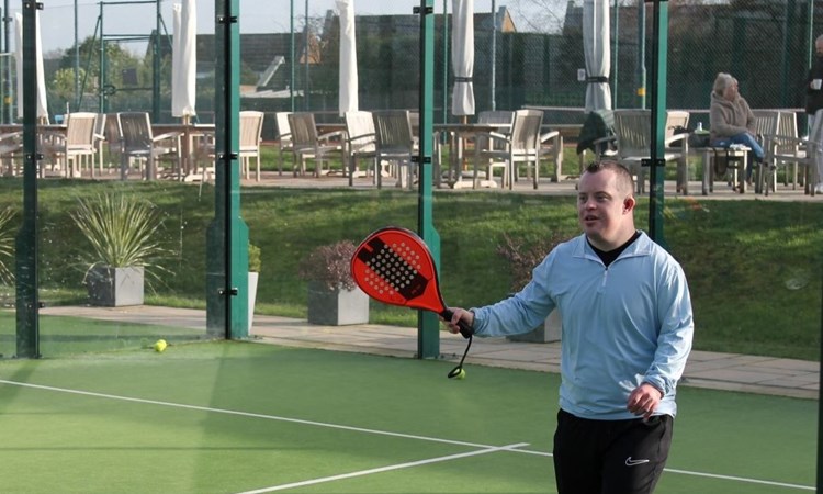 Young disabled man playing padel at a venue with a red padel bat