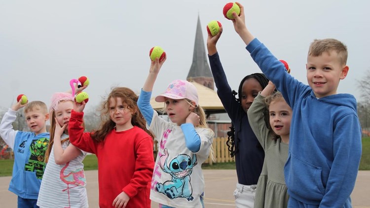 Primary school students standing in a line holding tennis balls in the air 