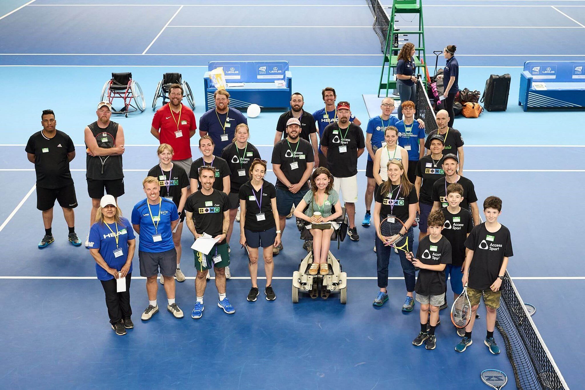A group of male and female volunteers on one side of a tennis court looking up at the camera, smiling
