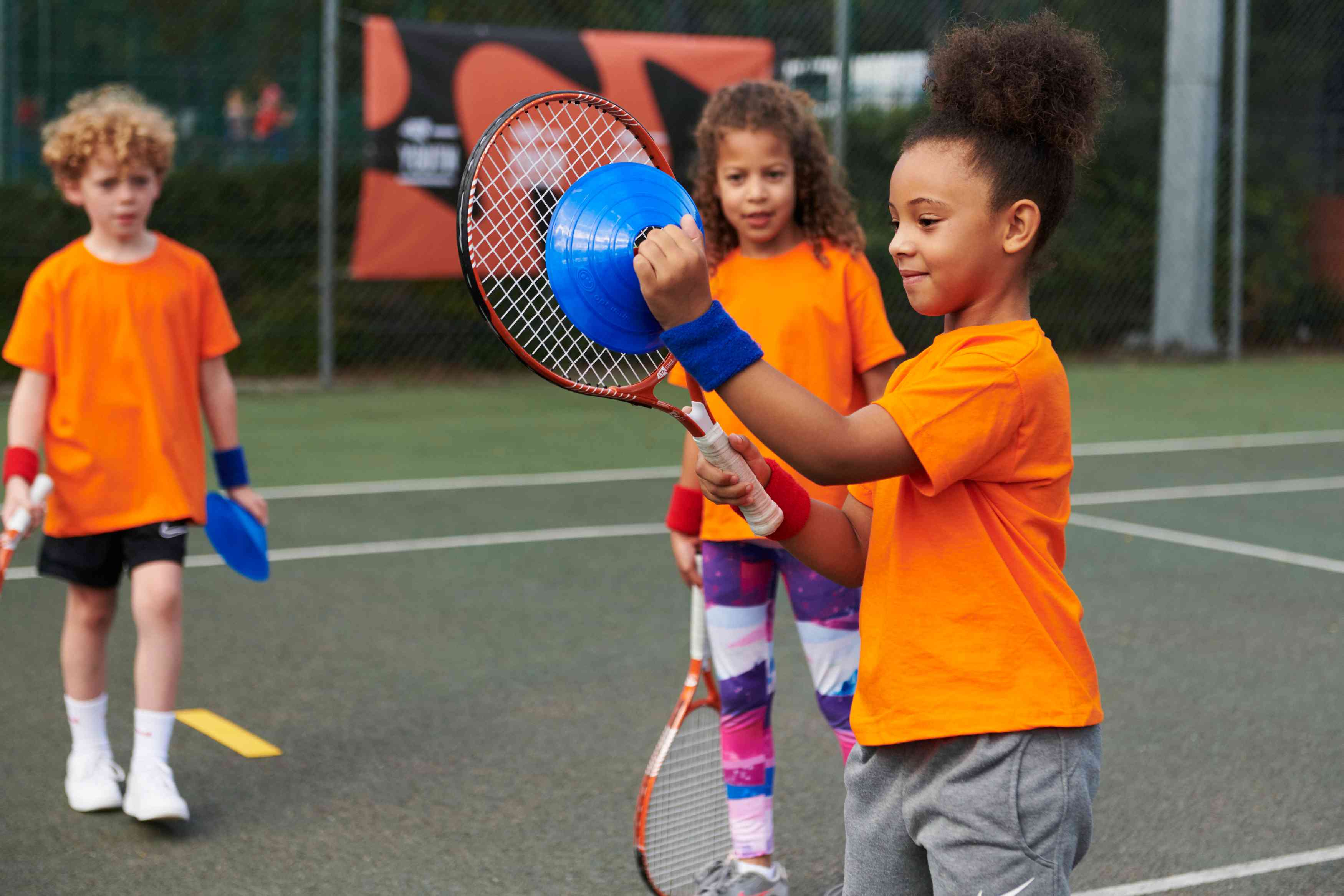 A child holding a tennis racket and cone on court