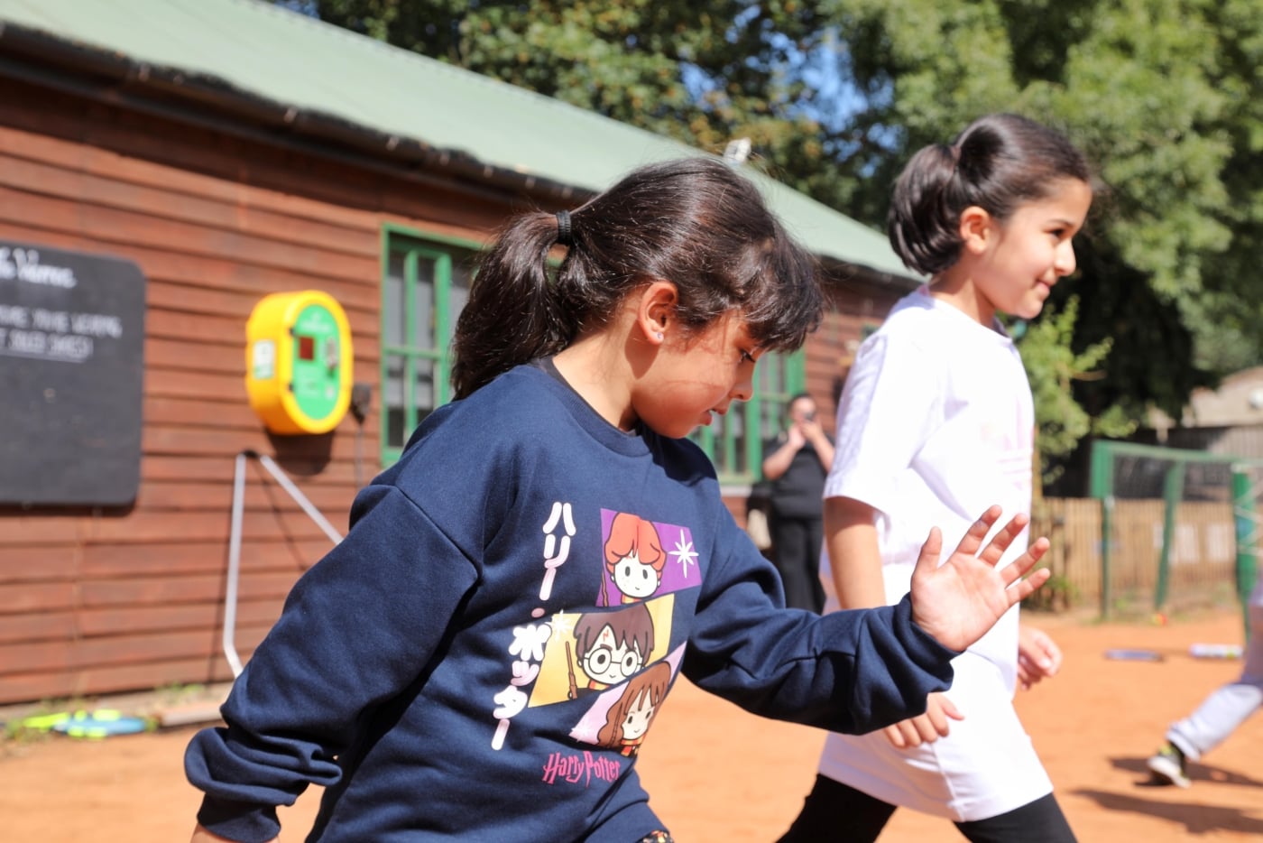 Two children stood, one has her hand lifted as though she is about to run