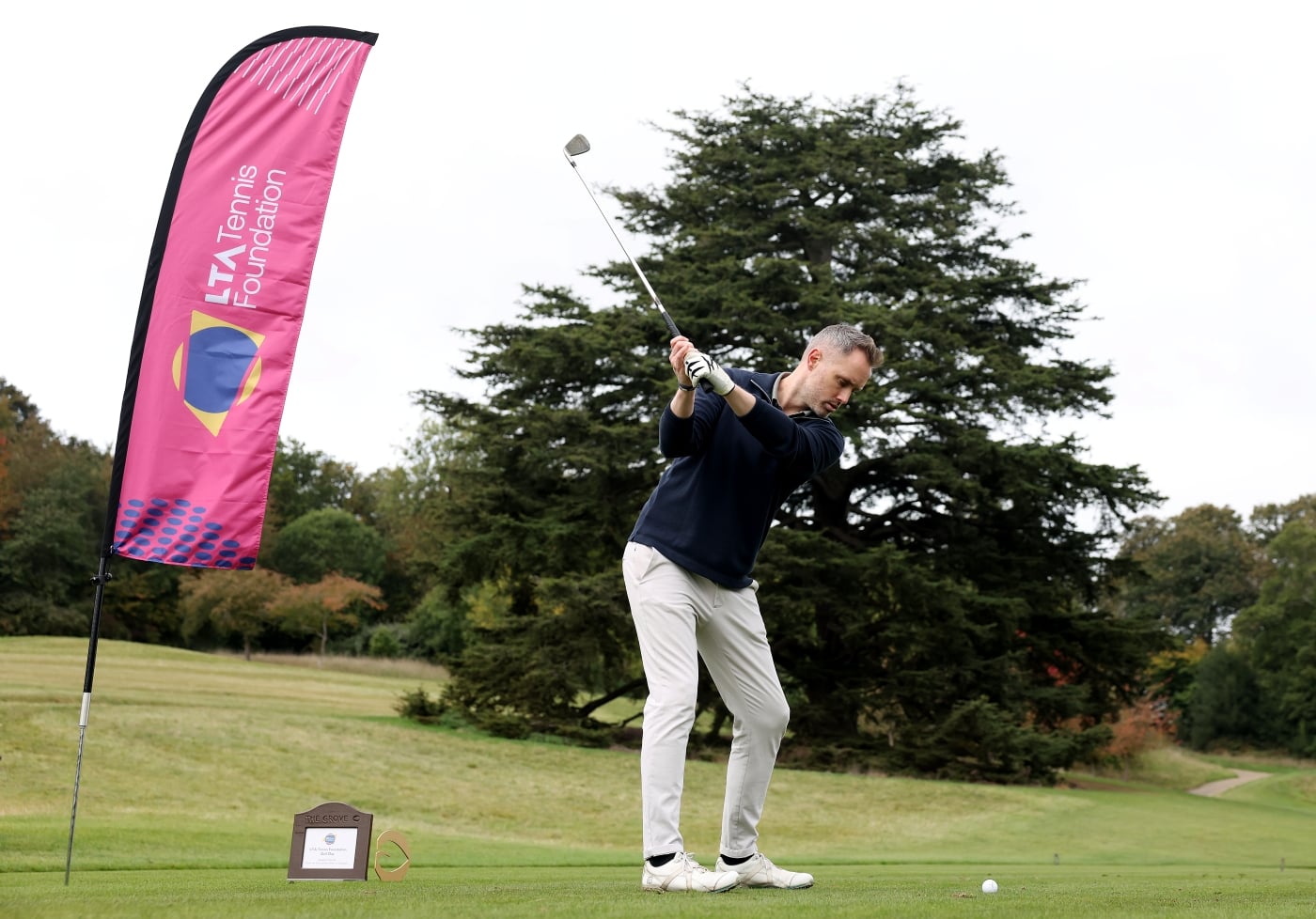 A man holding a golf club up, about to hit the ball