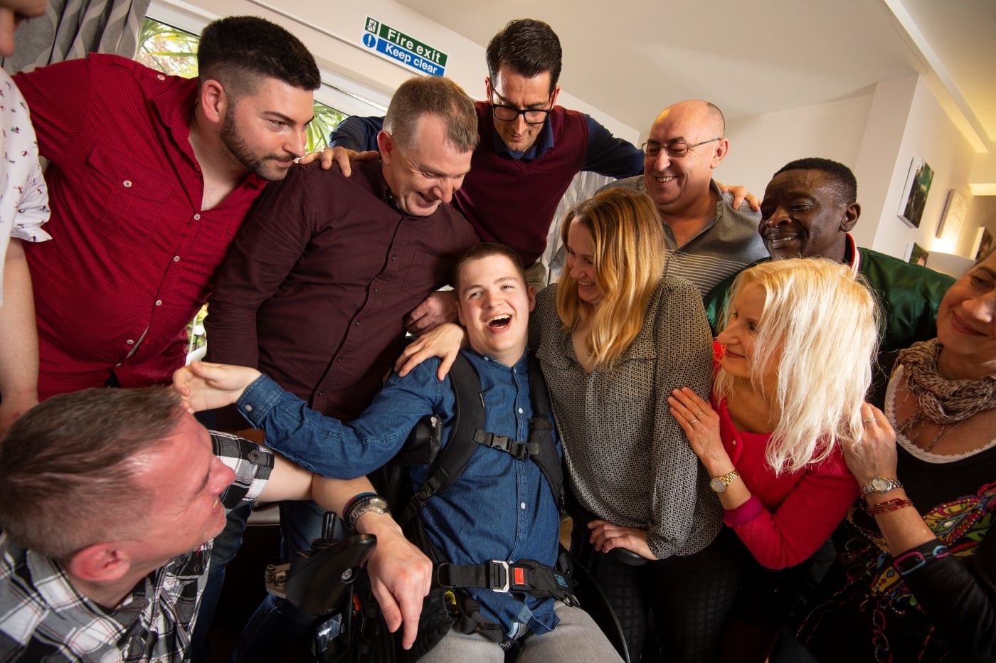 Disabled person in a wheelchair surrounded by group of people all smiling 