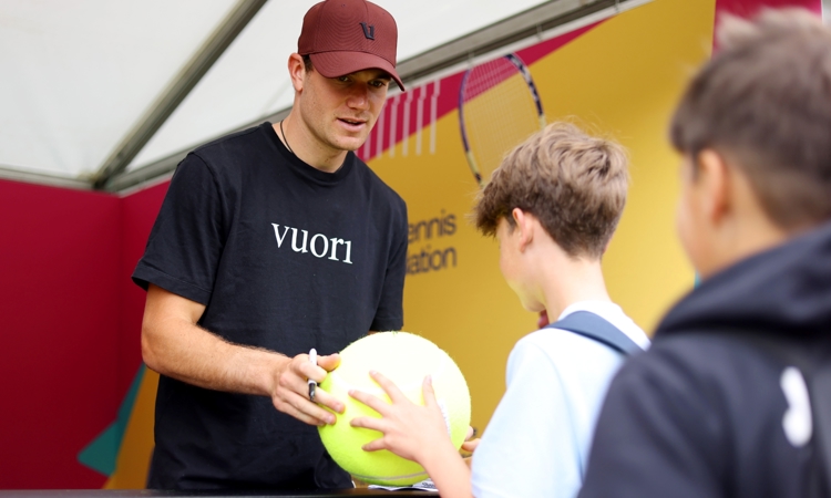Tennis player Jack Draper signing a large tennis ball for a young fan 