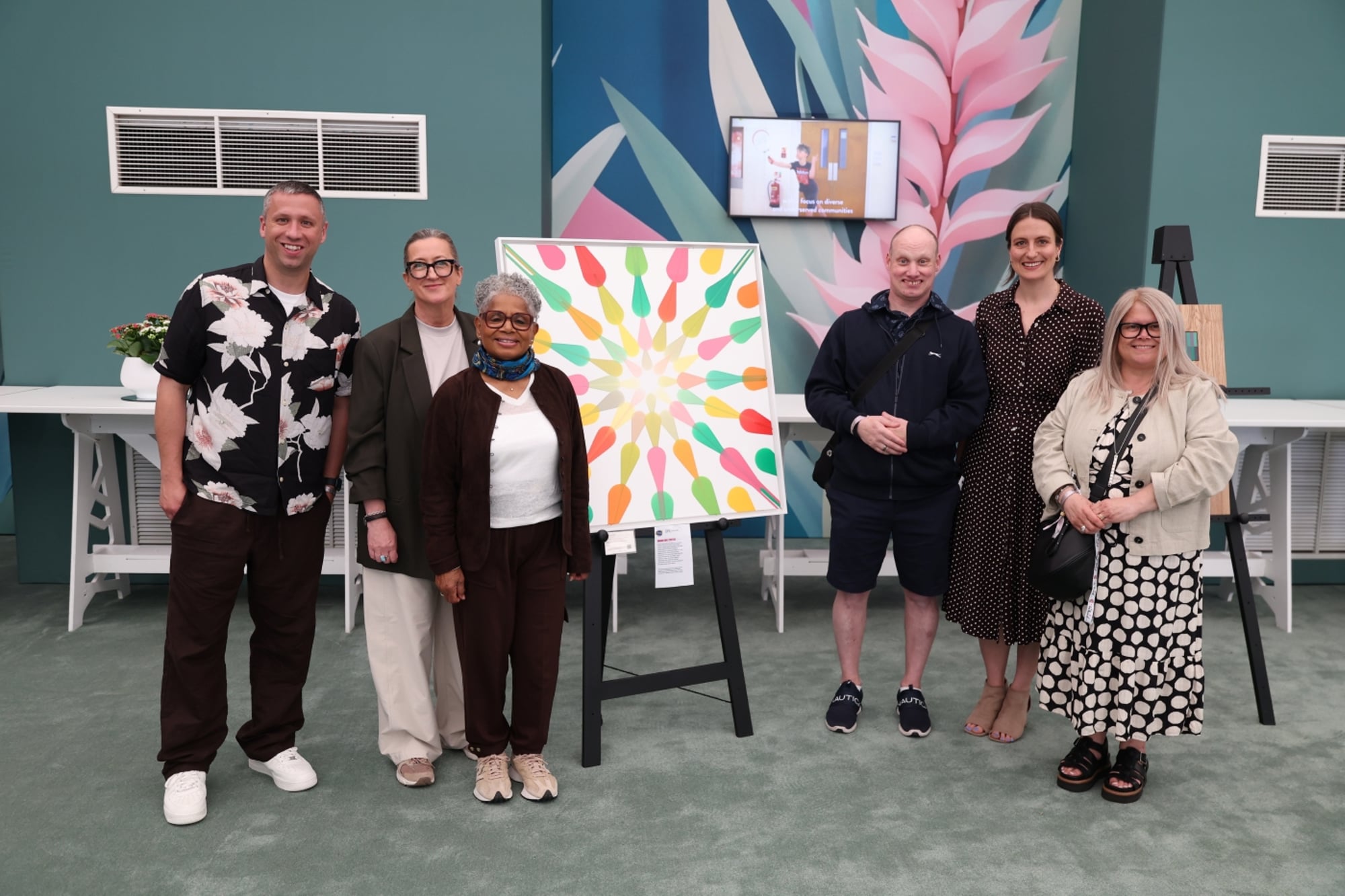 Six people looking at the camera next to a painting 