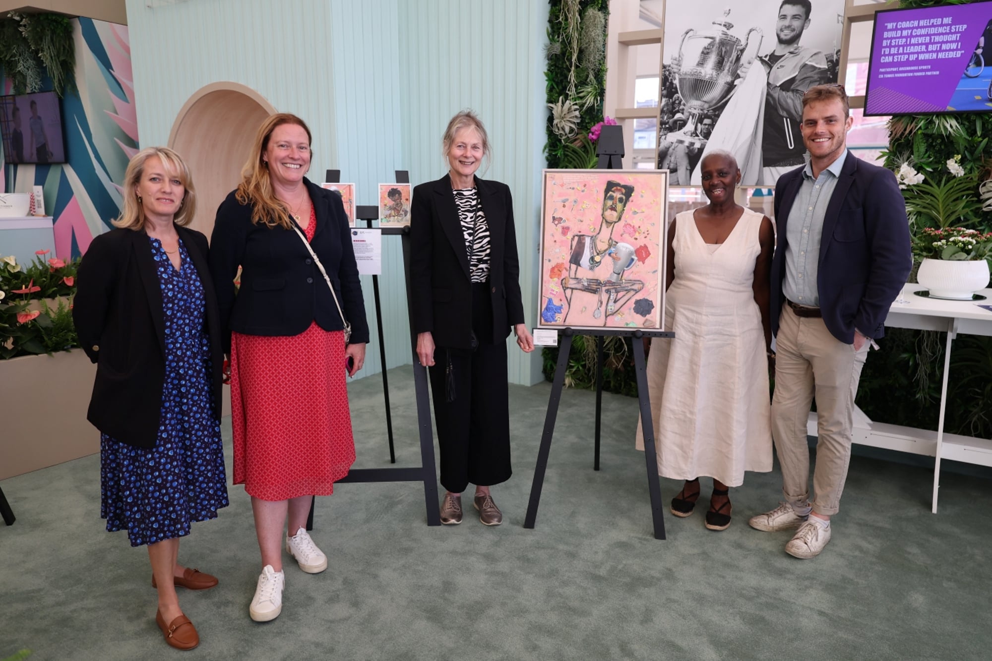 Five people looking at the camera next to paintings 