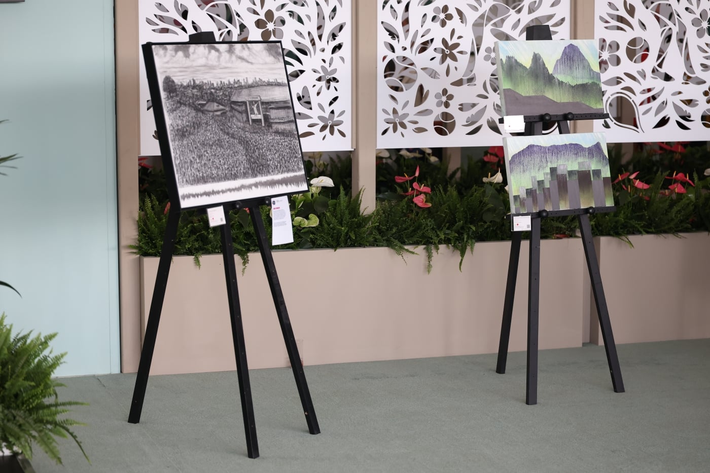 Three charcoal drawings on stands in a room 