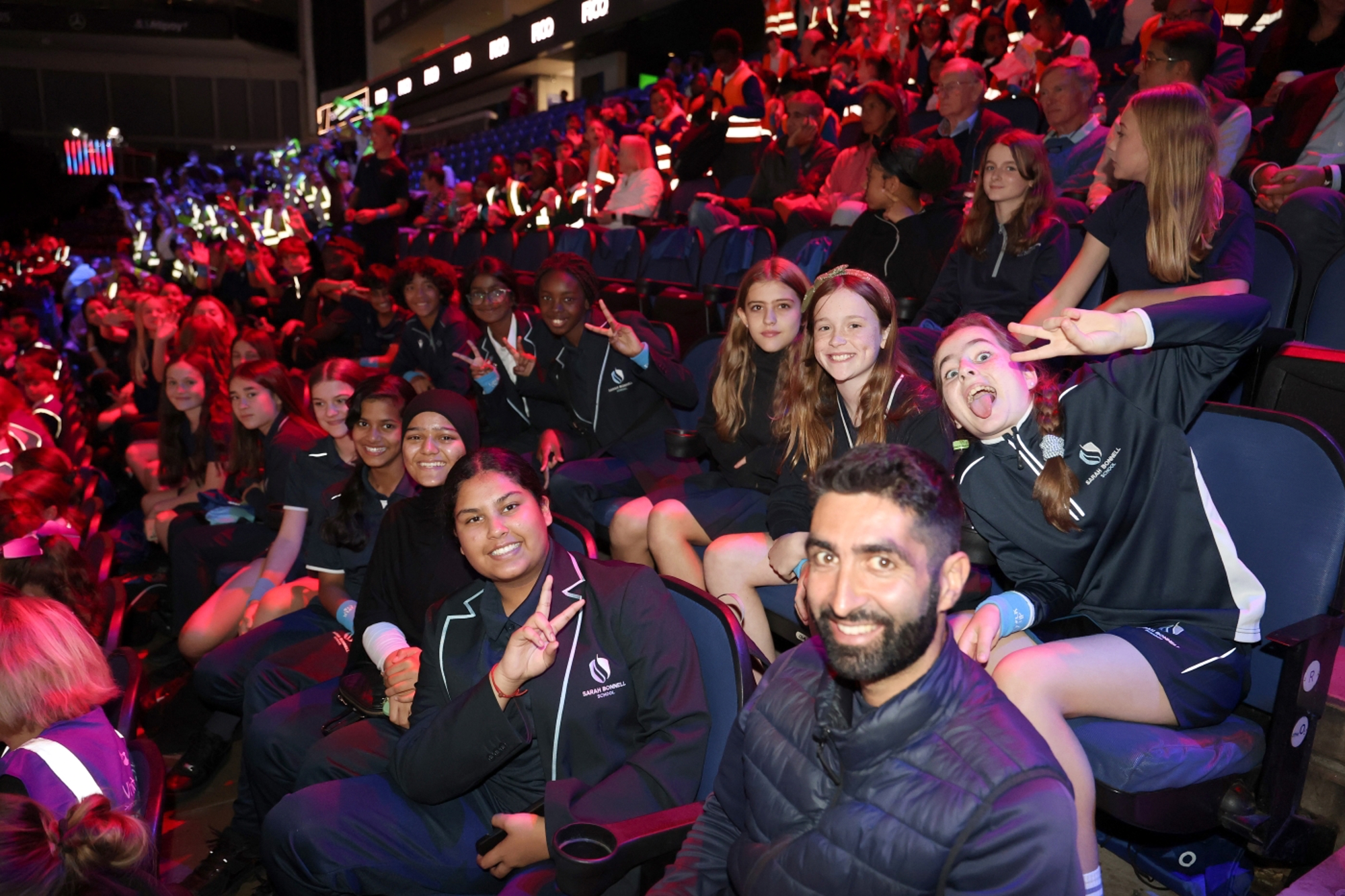 A group of secondary school aged children sitting in a stadium smiling at the camera 