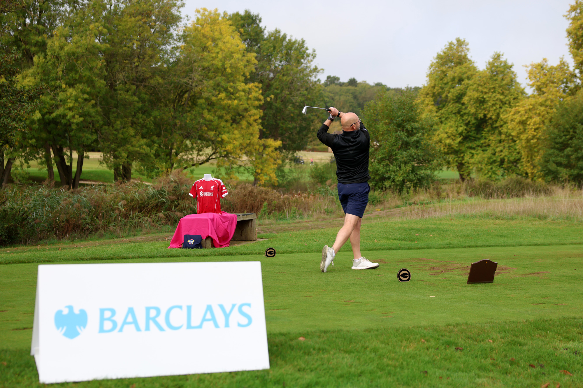 A man poses after hitting a golf ball with Barclays branding in front of him