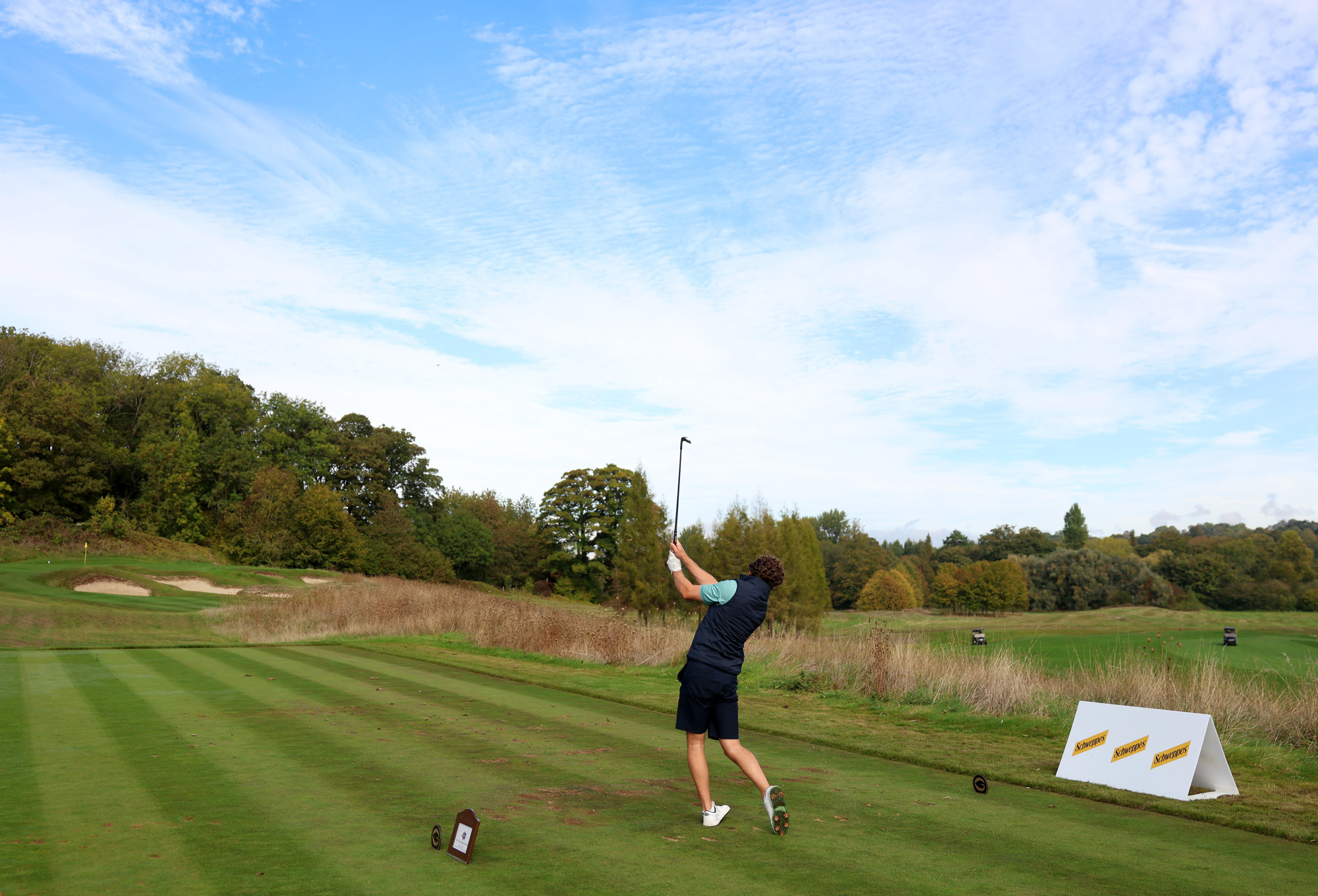 A man poses after hitting a golf ball with Schweppes branding in the background