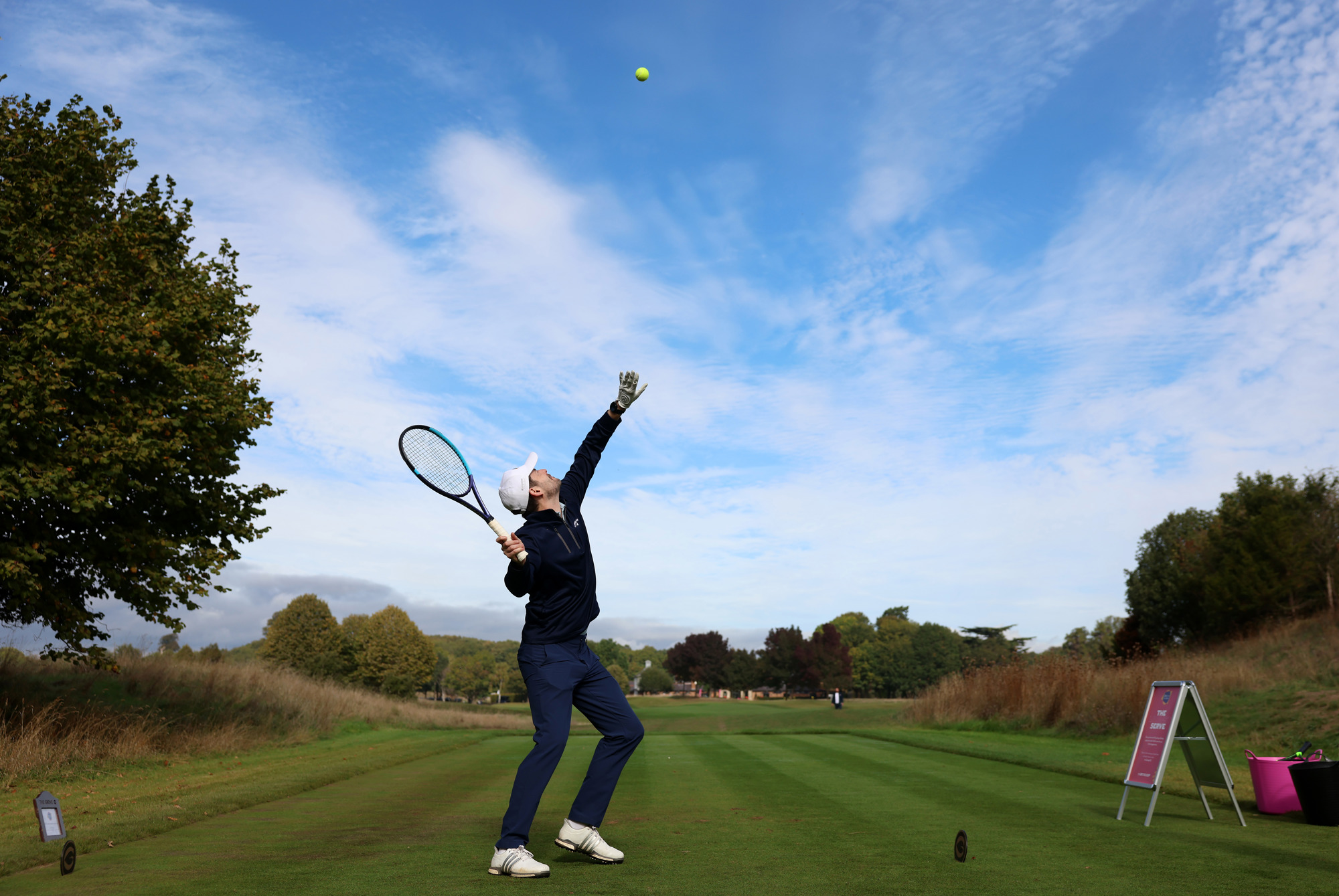A man serves a tennis ball on a golf course
