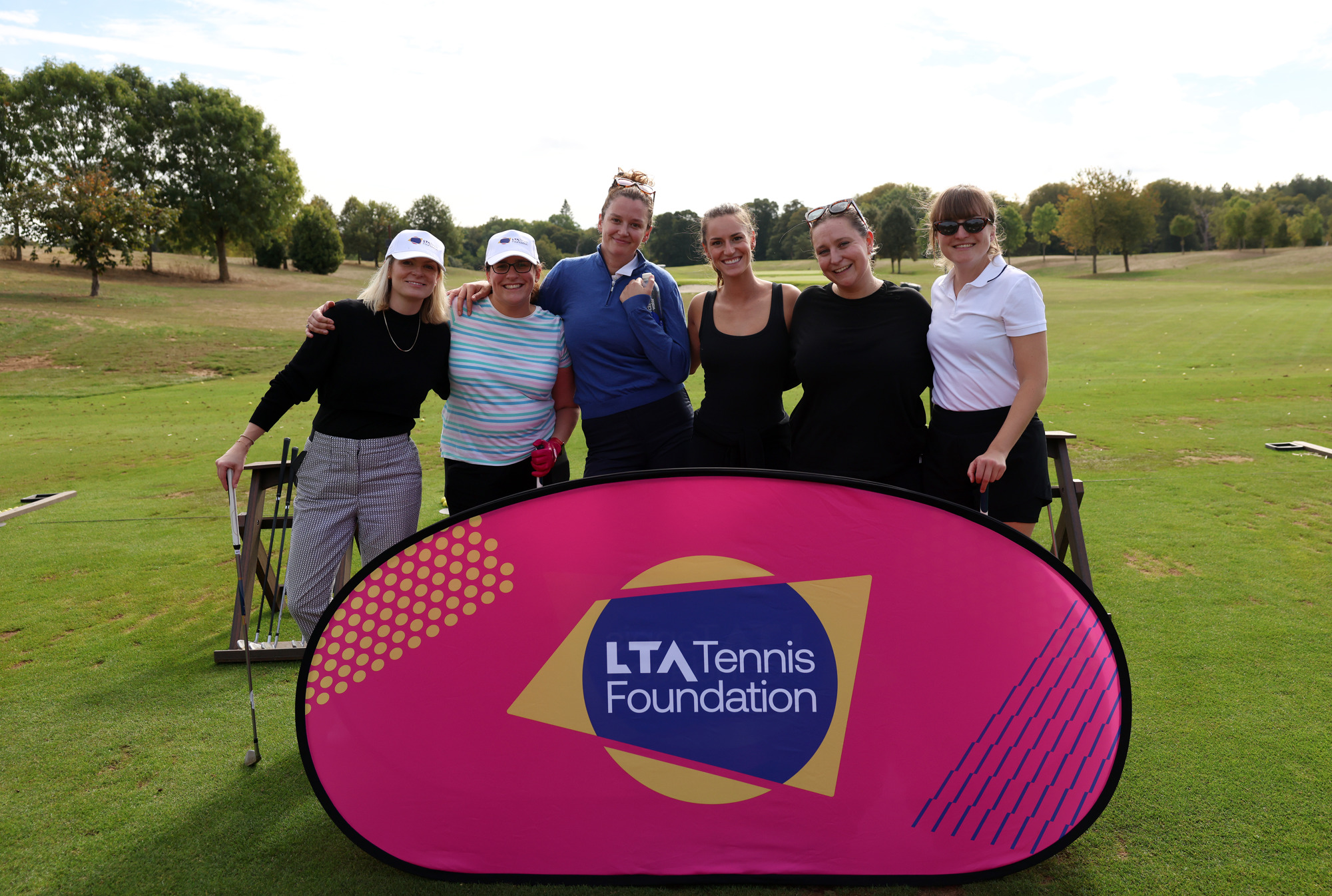 Six golfers gather around an LTA Tennis Foundation banner