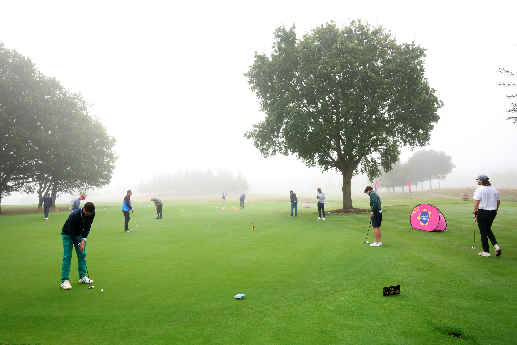 Several golfers practice putting with mist in the background