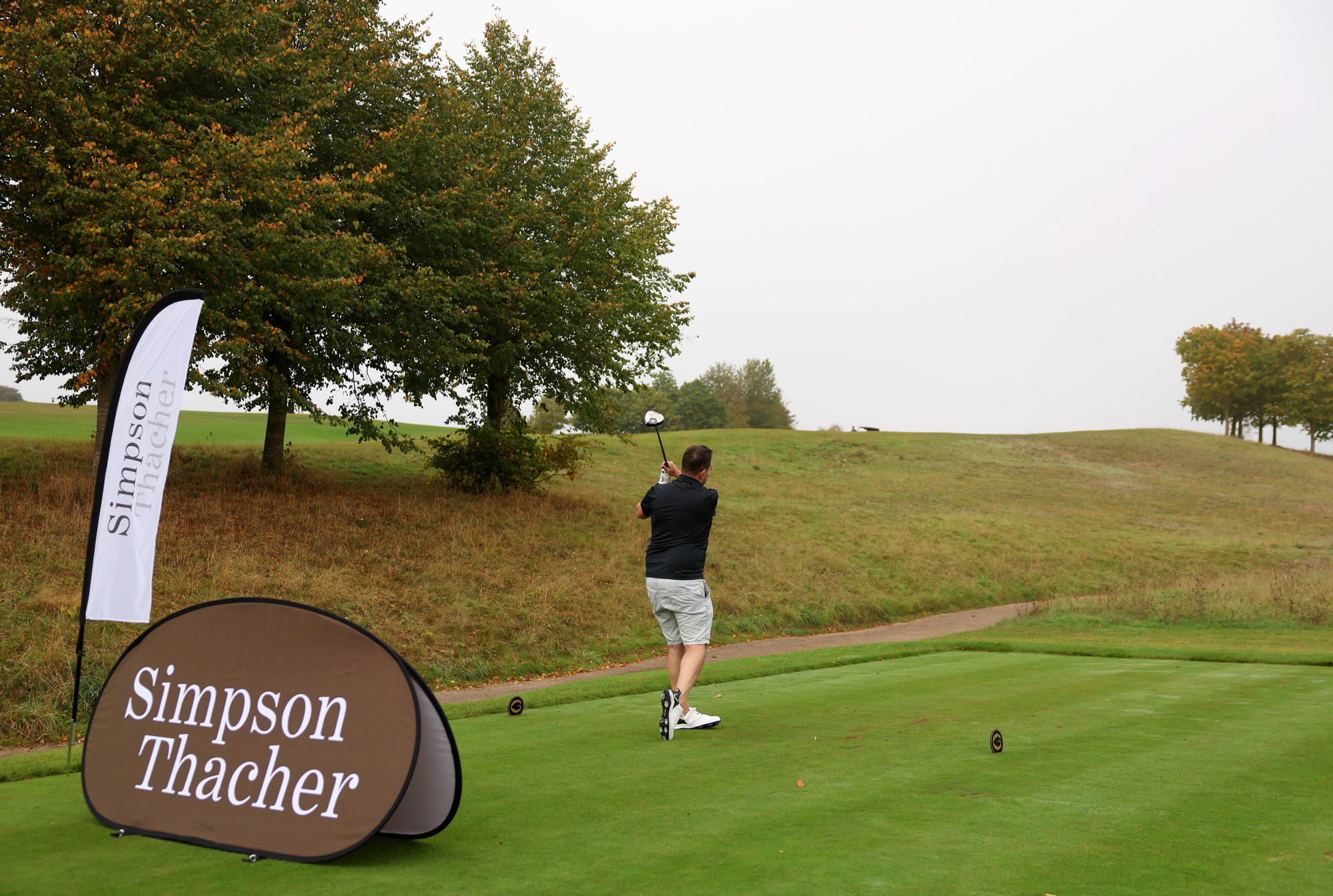 A man poses after hitting a golf ball with Simpson Thacher branding in front of him