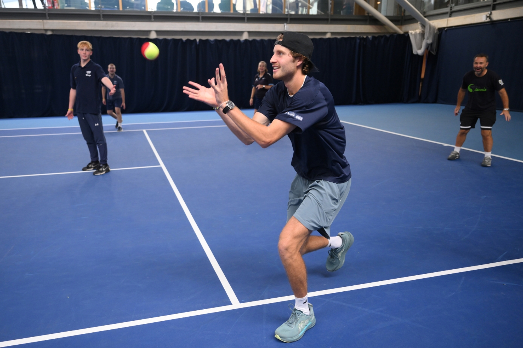 Professional tennis player Tobey Samuel catching a tennis ball on an indoor tennis court