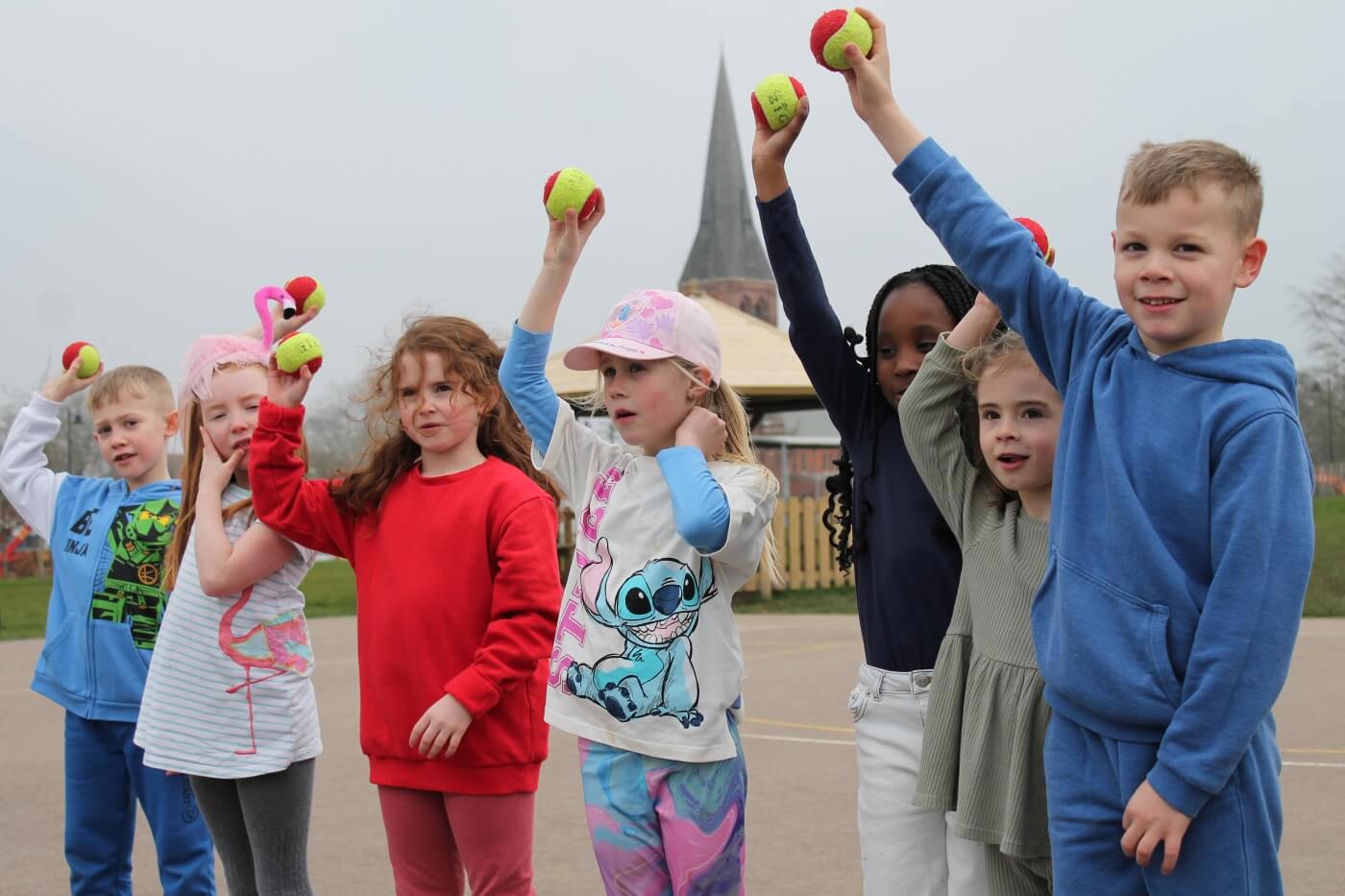 Primary school students standing in a line holding tennis balls in the air 