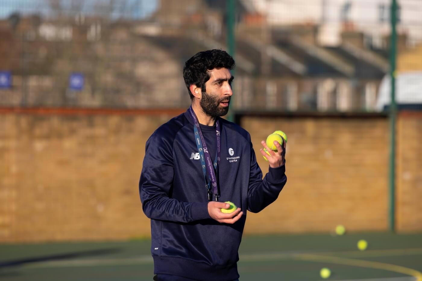 Greenhouse Sports Coach-Mentor holding tennis balls in hand on tennis court 