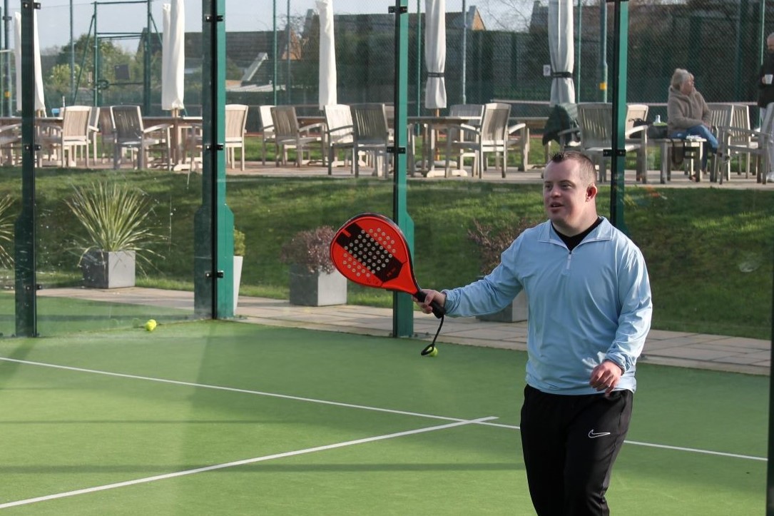 Young disabled man playing padel at a venue with a red padel bat
